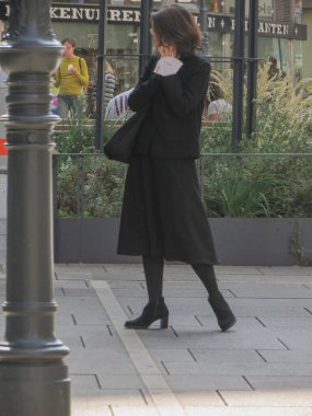 Vienna, AUSTRIA - CIRCA Eylül 2021: Siyah giyinmiş zarif bir kadın, arıyor ve yüz maskesi tutuyor.