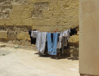 Giysiler kurumuş, eski bir duvarın yanında duruyor.