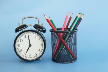 Mavi arkaplanda çalar saat ve kalemler