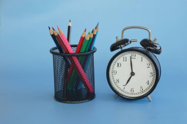 Mavi arkaplanda çalar saat ve kalemler