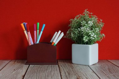 Çiçek saksısı ve kalemler masanın üstünde.