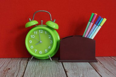 yeşil alarm saati ve kalemler masada.
