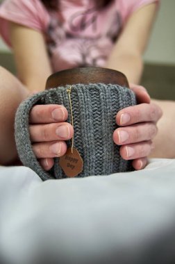 Sıcak bir sabah, bir fincan kahveyle yatakta. Kadın eli örülmüş bir kupayı tutuyor. Yakın plan..