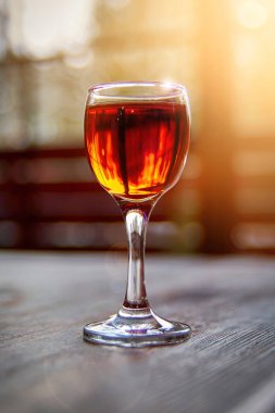 Glass of cognac on wooden table in the sunlight. Shot glass.
