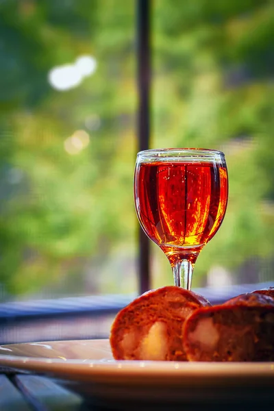 Glass of cognac on wooden table. on platter with sausages from wild game meat. — Foto de Stock