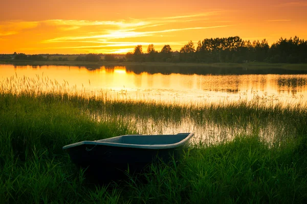 Boat on bank of river at sunset in grass — Stock Photo, Image
