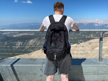 Gözlem güvertesinde duran ve dağların tepe ve bulutların muhteşem manzarasının tadını çıkaran bir turist..