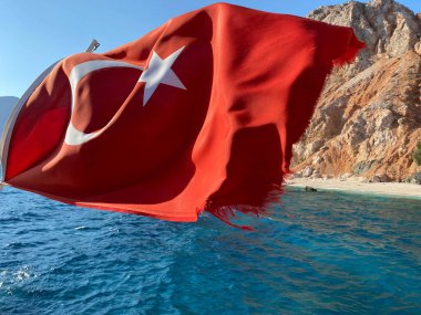 Deniz ve dağların arka planında güneşli havada Türk bayrağı.
