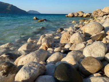 Büyük, güzel, doğal, yuvarlak taşlar ve çakıl taşları, deniz kıyısında ya da okyanusta, dağların arka planında suyla yıkanır..