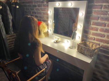 Kadın aynanın önünde makyaj yapıyor. Soyunma odası görünümünde..