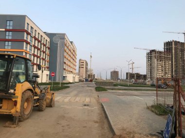 Bir asfalt kaldırım taşı, küçük bölgedeki yeni evlerin arka planına doğru ilerliyor. Arka planda yeni beton ve cam evler inşa ediliyor..