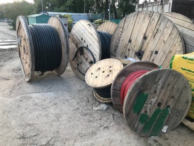 Büyük, ahşap, sarmalanmış siyah kabloyla bej makaralar. İnşaat halindeki yeni bir küçük bölge için şehir merkezinde iletişim kurulması.