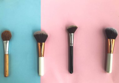 Pembe-mavi arka planda fırçalar. Makyaj, doğal temeli olan bir güzellik. Toz, temel, allık ve fosforlu kalem dağıtmak için fırça kullanın.