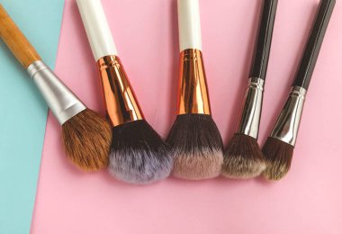 Fırçalar parlak bir arka planda yatar. Yüze doku uygulamak için doğal kıllarla kabarık fırçalar. Güzel yüz, göz farı için fırçalar, pudra ve allık..