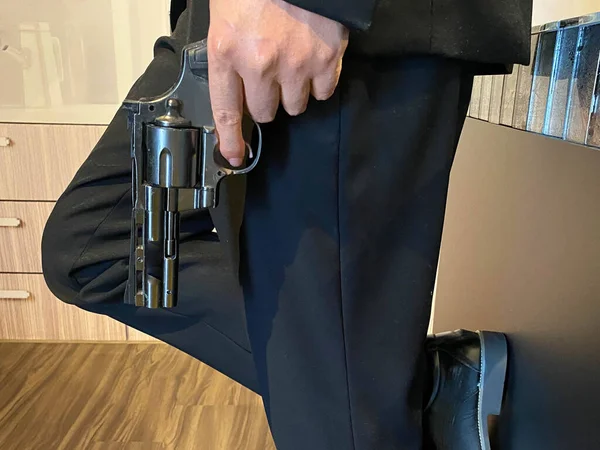 Close up on hand of unknown caucasian man holding a gun in by his leg while standing outdoor in sunny day - handgun criminal or self-defense concept with copy space.