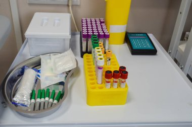Laboratuvar teşhisi. Çok renkli kapaklı test tüpleri tutacağında duruyor. Yanında iğneli ve nakil malzemeli bir tıbbi damar var. Damarları için turnike. Venöz kanı alıyor..