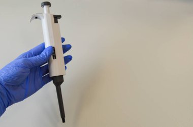 Laboratuvar analizleri için mekanik dağıtıcı. Dispanser mavi tek kullanımlık eldivenli bir doktor tarafından tutuluyor. Laboratuvar teşhisleri, hastalıkların tespiti için testler.