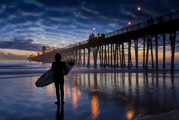 Surfař obdivovat západ slunce v blízkosti oceanside pier — Stock fotografie