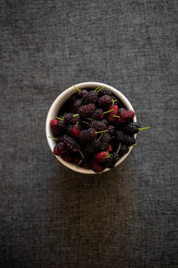 Masadaki kasede taze böğürtlen, yukarıdan bakıldığında koyu arkaplan, yukarıdan bakıldığında taze yaban mersinli beyaz kase, koyu arkaplan..
