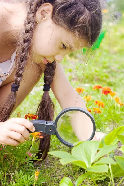 Girl sees flowers through magnifying glass — Stock Photo, Image