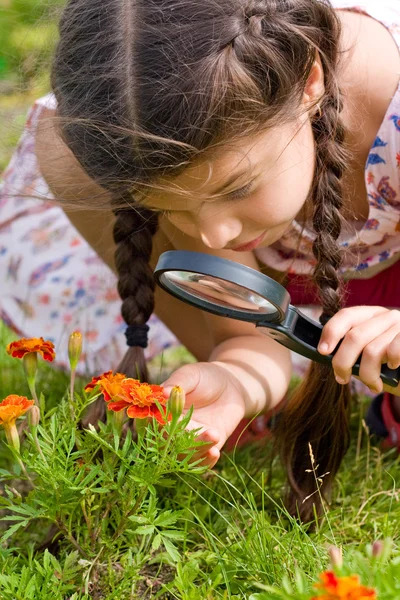 Girl sees flowers through magnifying glass — Stock Photo, Image