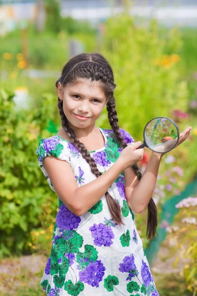 Girl looking through magnifying glass on flower — Stock Photo, Image