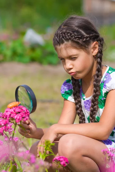 Girl looking through magnifying glass on flower — Stock Photo, Image