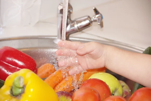 La mano del bambino sta giocando con acqua, verdure in un lavandino della cucina — Foto Stock
