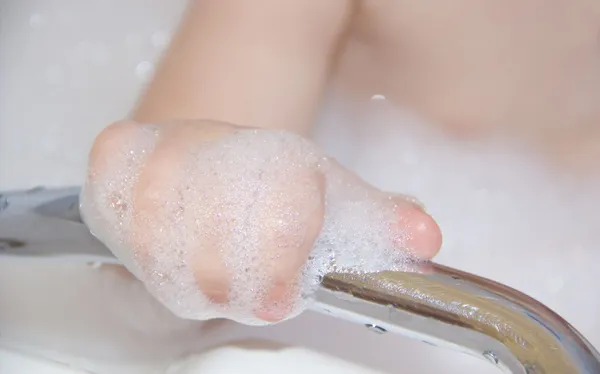 Mano del bambino di bagno in bolle di sapone si sta aggrappando alla rotaia — Foto Stock