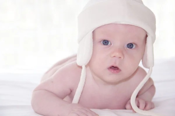 Cute little baby on tummy in white hat — Stock Photo, Image
