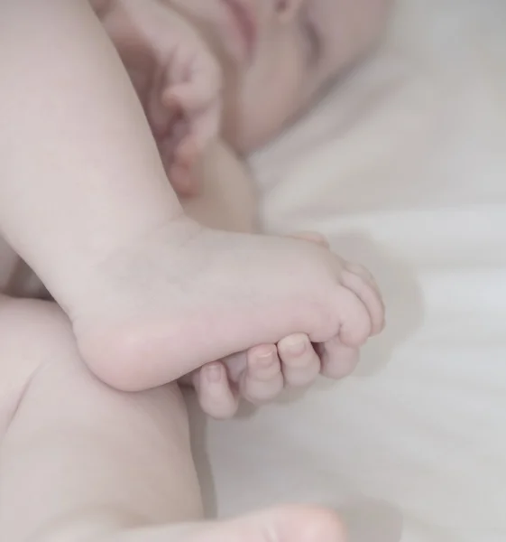 Hand van slapende baby houdt haar voet — Stockfoto