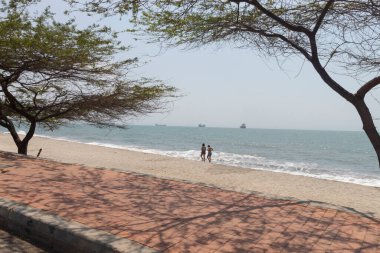 Santa Marta 'da yürüyen iki kadın, Kolombiya havaalanı plajında Karayip denizi ve arka planda büyük gemiler.