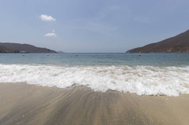 Güneşli bir günde siyah kum ve mavi okyanusla Kolombiya Tayrona doğal park plajı