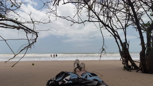 First person view of Colombian Palomino Beach landscape with branches trees, tourist and cloudy skyscapeat background