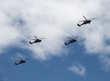 Four Black Hawk helicopters flying over crowd with blue and cloudy sky during colombian independence day military parade