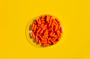 Sarı arka planda petri kabında turuncu kapsül hapları..