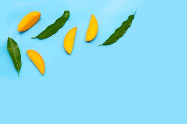 Tropikal meyve, mavi arka planda yapraklı mango dilimleri..