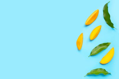 Tropikal meyve, mavi arka planda yapraklı mango dilimleri..