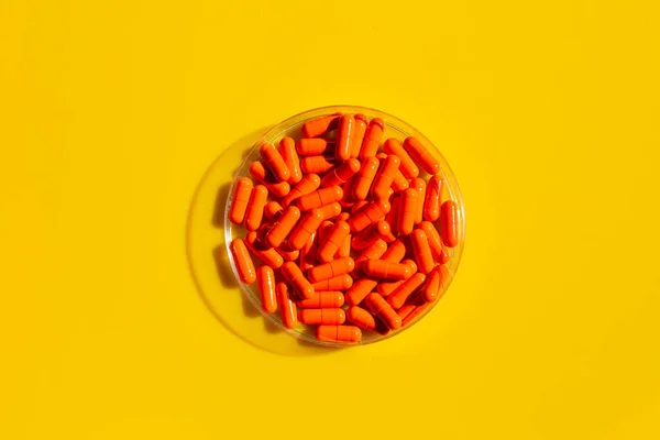 黄色の背景にペトリ皿のオレンジカプセル薬 — ストック写真