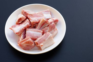 Beyaz tabakta, koyu arkaplanda çiğ domuz kaburgası..