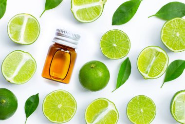 Beyaz arka planda taze limon ve yeşil yapraklı gerekli yağ şişesi. Üst görünüm