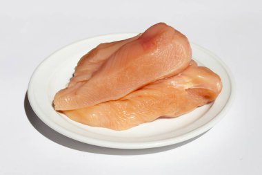 Pişmemiş çiğ tavuk göğsü fileto beyaz tabakta beyaz arka planda.