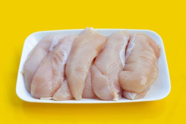 Sarı arka planda beyaz tabakta çiğ tavuk eti..