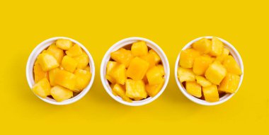 Tropikal meyve, mango küp dilimleri sarı arka planda beyaz bardaklarda.