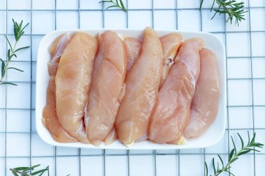 Beyaz arka planda tabakta çiğ tavuk ihaleleri.