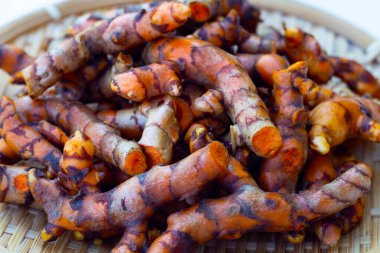 Beyaz zemin üzerinde ahşap kaşık üzerinde zerdeçal kökleri.