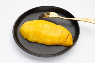 Beyaz arka planda siyah tabakta sarı mango dilimleri.