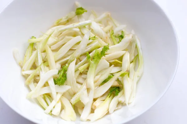 Sliced fresh fennel in white bowl on white background.