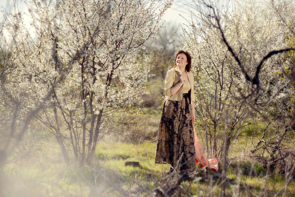 In the garden with flowering trees posing woman with a scarf in a long skirt