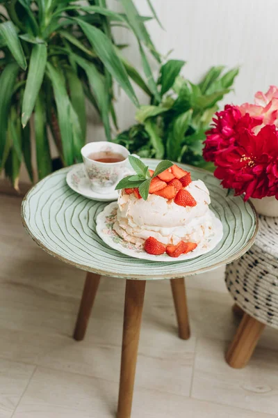 小さなテーブルの上の家庭の植物の背景にクリームとイチゴのデザートケーキ — ストック写真